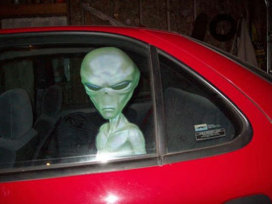 alien ridding the back seat of a red car